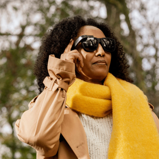 A photo of Yet wearing the Envision Glasses with the Smith Optics frames. She's wearing a yellow scarf and in the background there are trees.