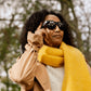 A photo of an Envisioners who's wearing and interacing with the Envision Glasses with the Smith Optics Frames. She's wearing a yellow scarf and there are trees in the background.